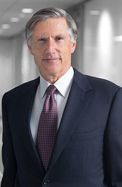 Bruce A. Karsh, smiling wearing a blue suit with a white shirt and red and gray tie. 