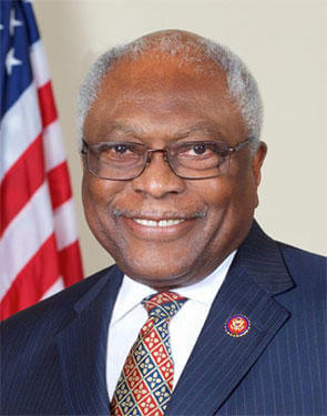 The Honorable James E. Clyburn wearing a pin-striped blue suit with a red and blue tie and the US Flag in the background.