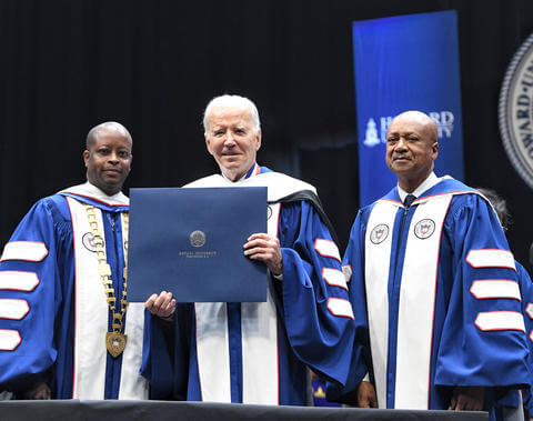 President Joe Biden holding an award and standing beside President Fredrick and Chairman Morse wearing blue graduation regalia.