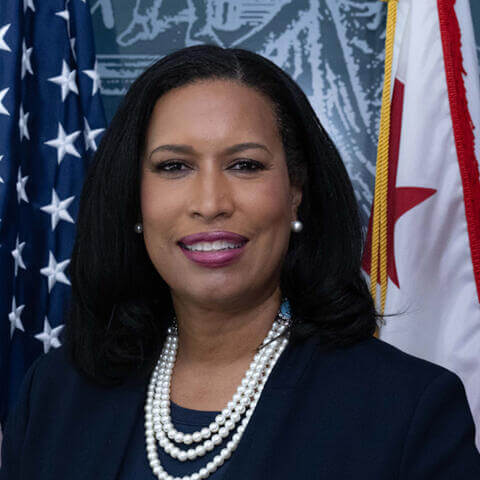 The Honorable Muriel Bowser smiling next to the American flag and the Washington, D.C. flag